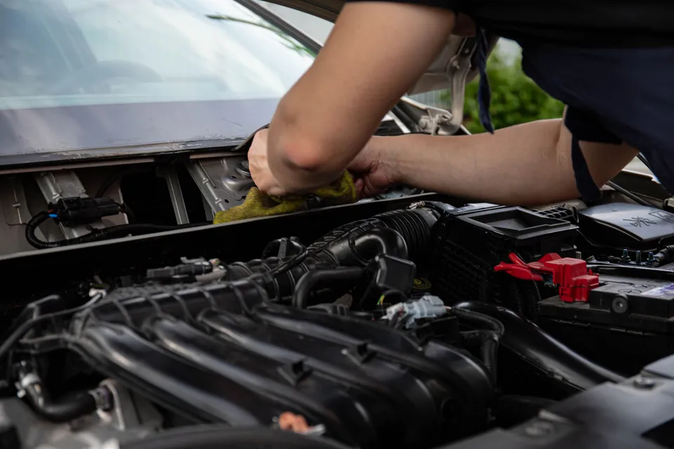 Ręce mechanika nad otwartą maską auta, w jasnym świetle dziennym widać komorę silnika