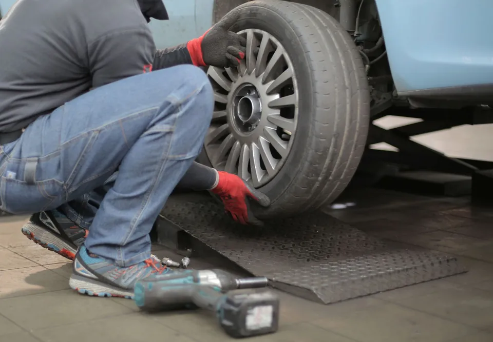 Mechanik zdejmuje koło auta, na posadzce leży klucz udarowy